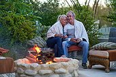 Happy senior couple sitting and drinking wine at fire pit on patio
