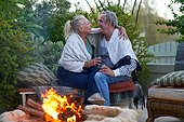 Happy senior couple drinking wine and hugging by fire pit on patio