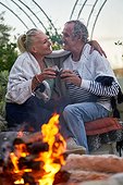 Happy senior couple hugging and drinking red wine by fire pit on patio