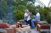 Happy senior couple drinking wine by fire pit on garden patio