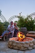 Happy senior couple drinking wine by fire pit on summer patio