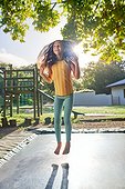 Carefree, barefoot girl jumping on trampoline in sunny backyard