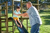 Father playing with son with Down Syndrome on slide in sunny backyard