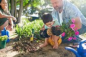 Father helping son with Down Syndrome planting flowers in garden