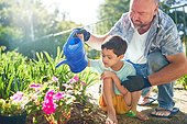 Father and son with Down Syndrome watering flowers in sunny garden