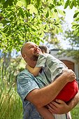 Happy father holding, hugging son under tree in summer backyard