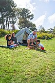 Happy family camping, stacking firewood outside tent in sunny grass