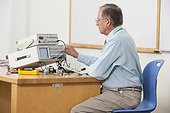 Professor adjusting oscilloscope triggering level in electronics classroom