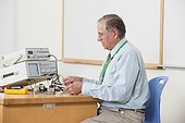 Professor wiring oscilloscope connections in electronics classroom