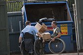 Men in wheelchairs throwing garbage into a trash dumpster