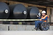 Facilities engineer in a wheelchair pulling caution tape in front of chemical storage tanks