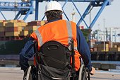 Transportation engineer in a wheelchair inspecting shipping containers and container cranes at shipping port