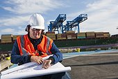 Transportation engineer in wheelchair with ear protectors studying plans at shipping port