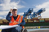 Transportation engineer in a wheelchair studying plans at shipping port