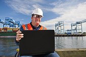 Transportation engineer in wheelchair recording data on laptop at shipping port