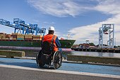 Transportation engineer in wheelchair inspecting container ship at shipping port