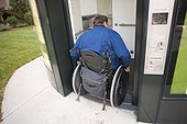 Man in wheelchair with spinal cord injury entering a public pay toilet