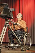 Man in wheelchair with muscular dystrophy using a TV camera and a teleprompter in studio