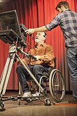 Man in wheelchair with muscular dystrophy at a TV camera with producer in a TV studio