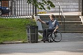 Man with spinal cord injury in a wheelchair putting trash in receptacle at public park