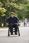 Man with spinal cord injury in a wheelchair maneuvering wheelchair quickly on path through public park