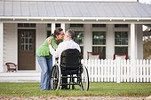 Couple kissing in front of their new home while he is in a wheelchair