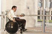 Businessman with spinal cord injury in wheelchair using automatic door opener at office building entrance