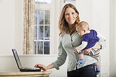 Woman working on a computer at home while holding baby