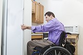 Man in wheelchair with spinal cord injury opening a refrigerator in an accessible kitchen