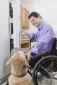 Man in wheelchair with spinal cord injury opening a refrigerator and petting his service dog