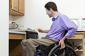 Man in wheelchair with spinal cord injury dusting in an accessible kitchen