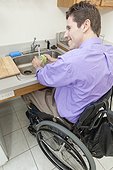 Man in wheelchair with spinal cord injury washing glass in an accessible kitchen sink