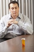Businessman at desk looking at a pill bottle