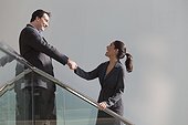 Hispanic businesswoman shaking hands with businessman on stairwell in office building