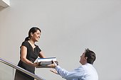 Business couple passing folders on stairs of office building