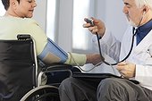 Doctor with muscular dystrophy in wheelchair checking the blood pressure of a patient