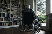 Senior man in wheelchair looking out through window