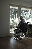 Senior man in wheelchair looking out through window