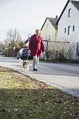 Old woman walking with pet dog on street