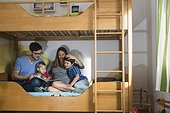 Father and the pregnant mother reading a book to their two sons on bunkbed, Munich, Germany
