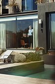 Businessman talking on smart phone at sunny, luxury patio window