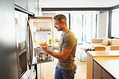 Man holding orange juice at open refrigerator in kitchen