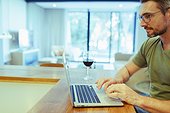 Man using laptop and drinking wine, working from home in kitchen