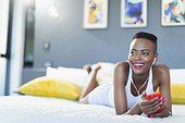 Smiling young woman relaxing on bed, listening to music with mp3 player and headphones