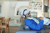 Happy man with headphones listening to music on living room sofa