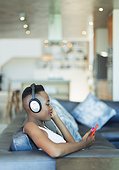 Young woman listening to music with headphones and mp3 player on sofa