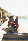 Woman sunbathing, reading book on sunny lounge chair at poolside