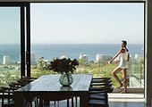 Young woman standing on modern balcony with sunny ocean view