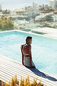 Serene young woman at sunny rooftop swimming pool