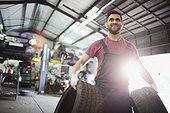Portrait smiling male mechanic carrying tires in auto repair shop